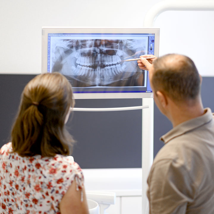 Zahnarzt erklärt einer Patientin ein Röntgenbild.
